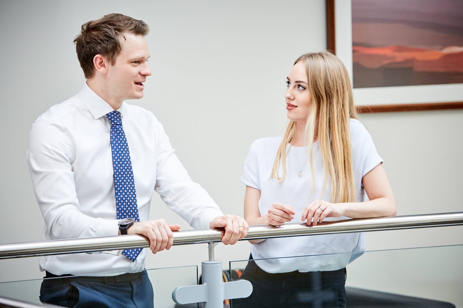 Male and female colleagues stood talking in communal area